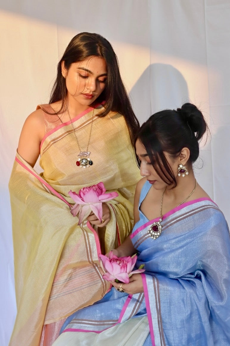Two women in traditional blue and yellow sarees holding pink flowers